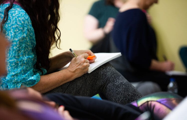 A student learning yoga therapy is writing into their notebook